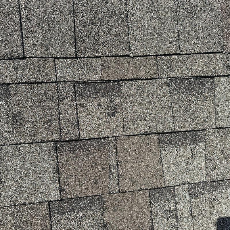 Asphalt shingle roofing surface with visible wear spots Asphalt shingle roofing surface with visible wear spots
