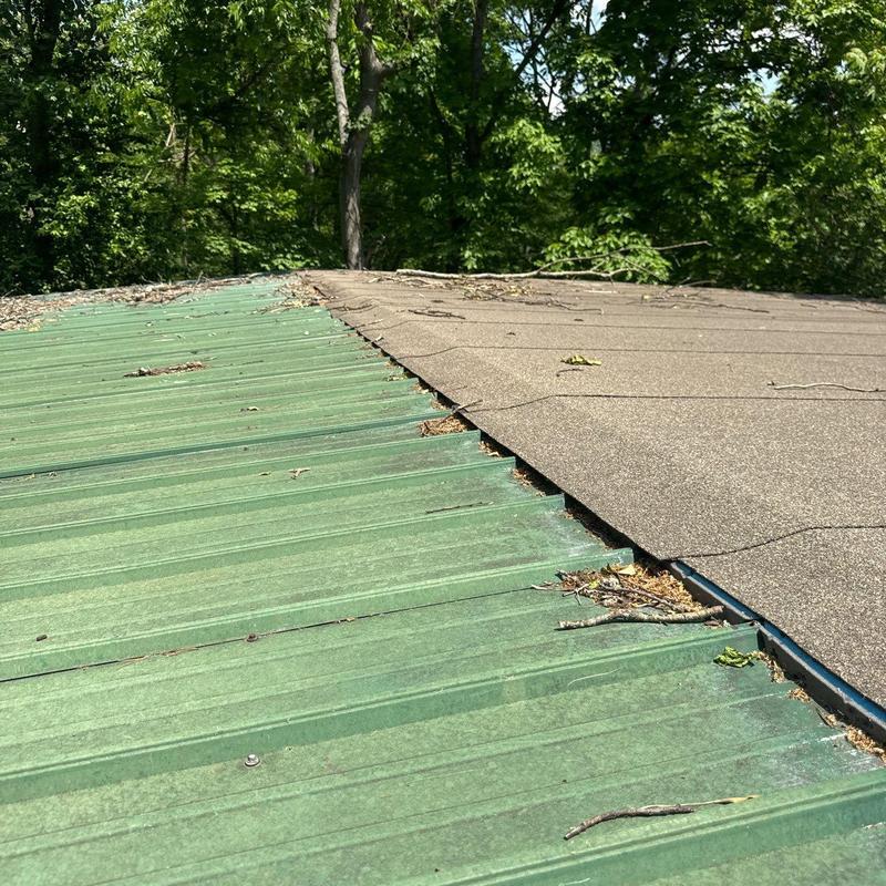 Metal roofing panel and shingle roof overlap with debris