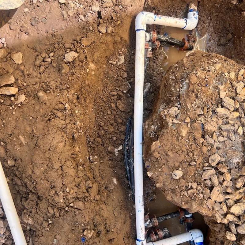 Irrigation lines rerouted around concrete post in soil trench