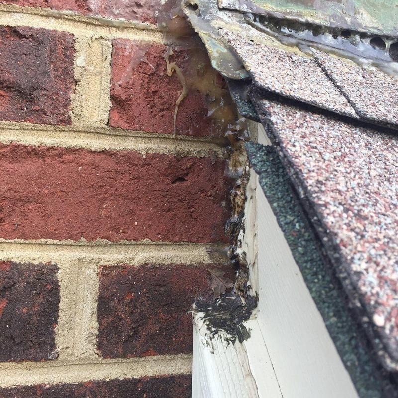 Roof shingles and flashing with sealant damage near brick wall