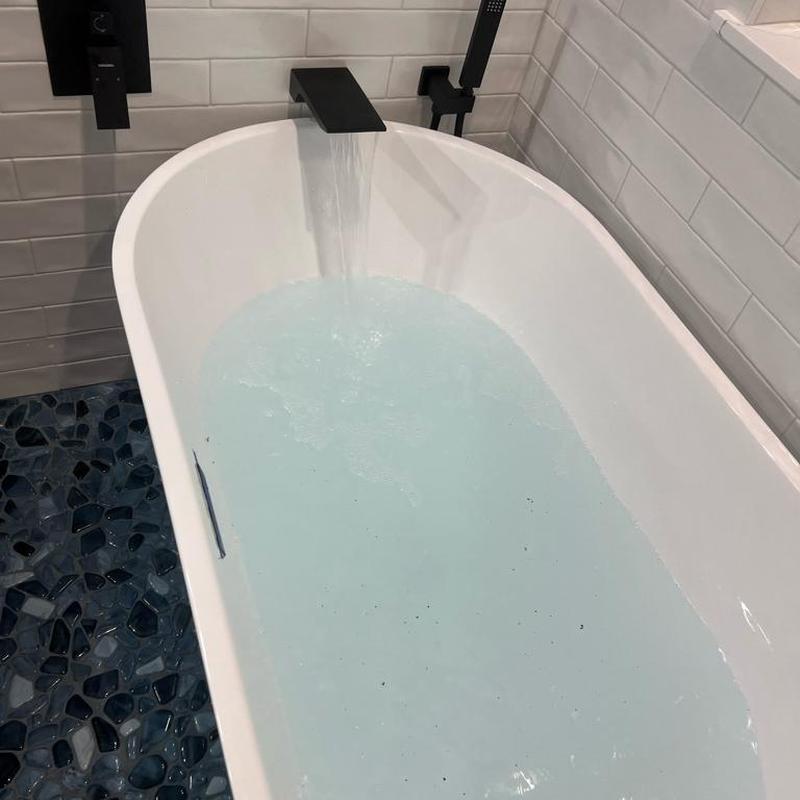 Freestanding bathtub filling with water and black faucet
