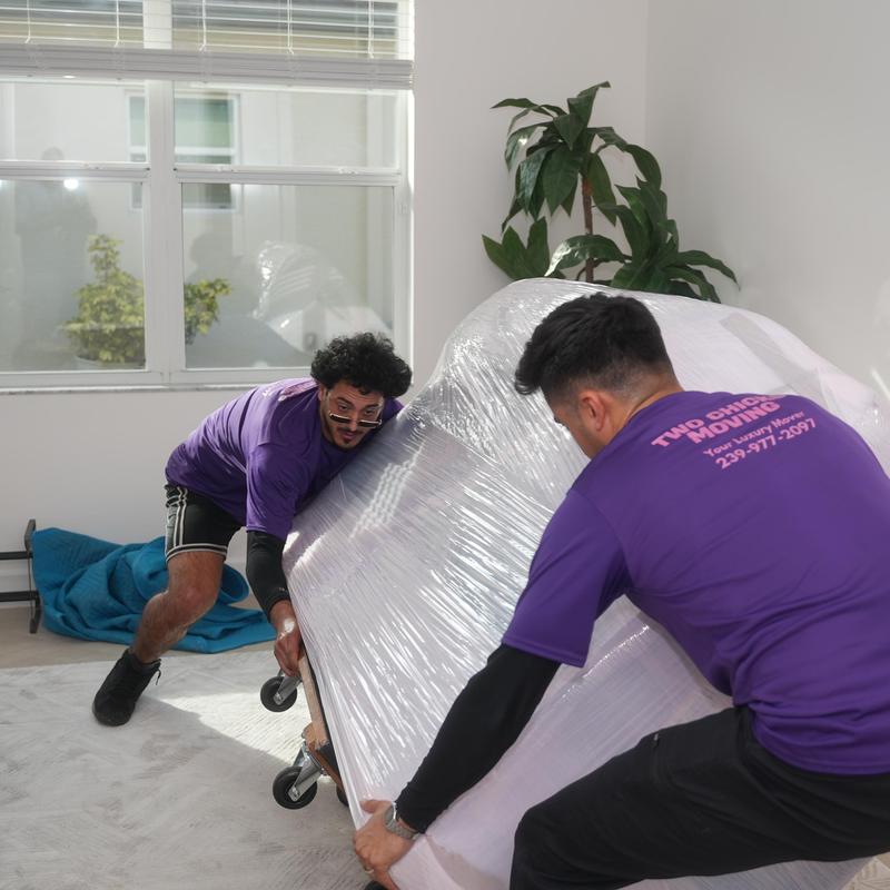 Sofa wrapped in plastic being moved by two workers