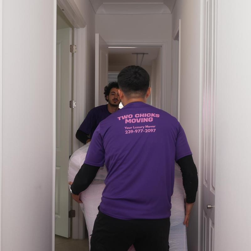 Furniture moving team carrying wrapped couch through hallway