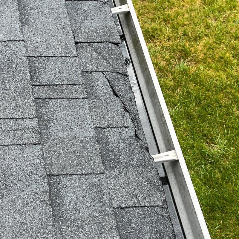 Asphalt roof shingles with visible damage near gutter edge