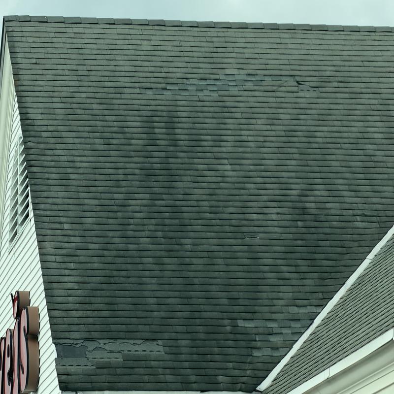 Commercial asphalt shingle roof with wind damage and wear Commercial asphalt shingle roof with wind damage and wear