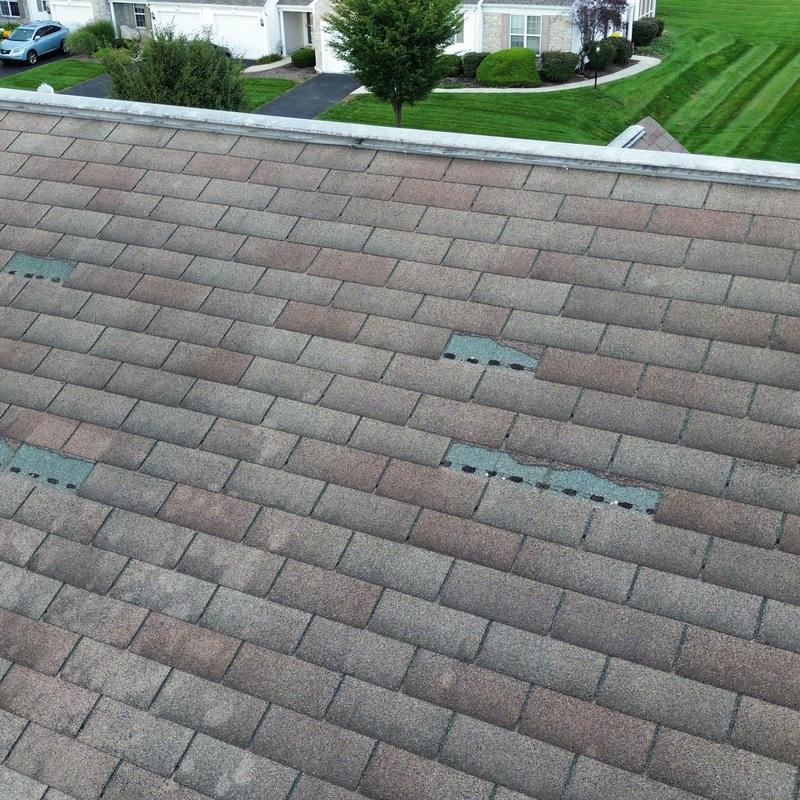 Asphalt shingles with wind damage on roof slope Asphalt shingles with wind damage on roof slope