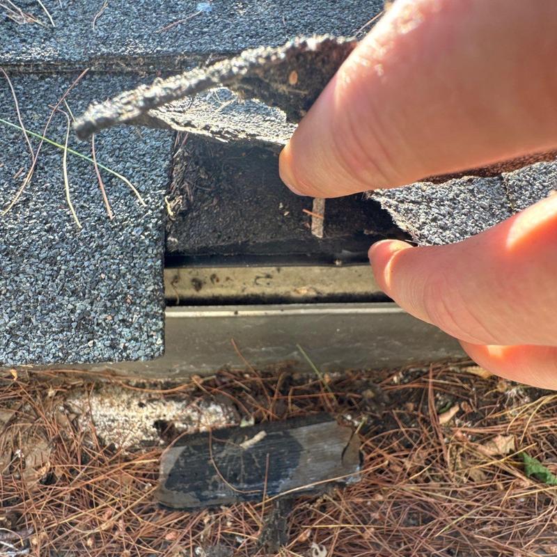 Roof shingles lifted showing underlying damage and debris