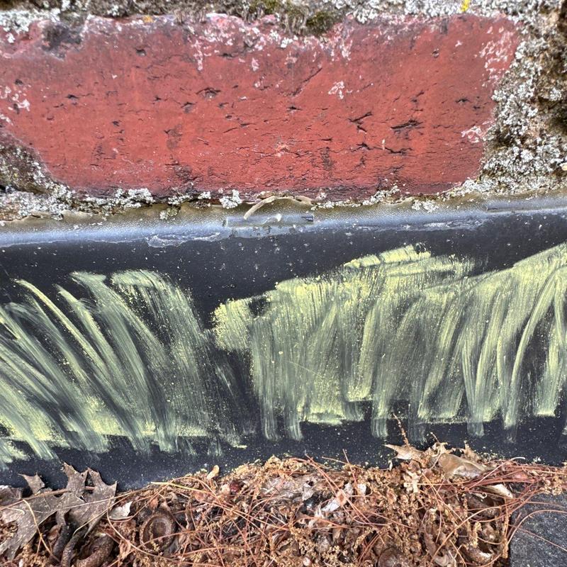 Metal drip edge with chalk markings near brick wall