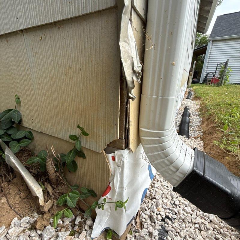 Vinyl siding corner damaged near white downspout drainpipe