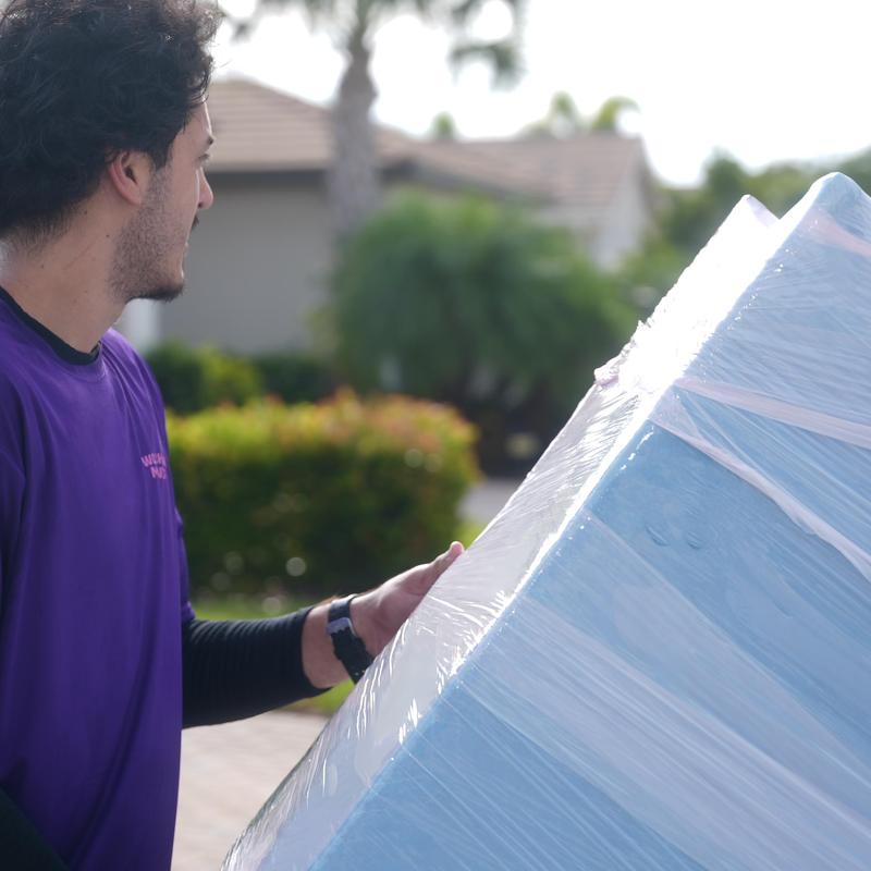 Mattress wrapped in plastic being moved outdoors