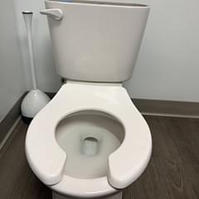 Toilet with open front seat and plunger nearby