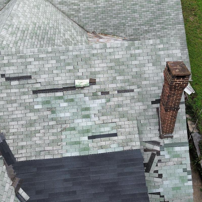Asphalt shingle roof with wind and patch damage near chimney Asphalt shingle roof with wind and patch damage near chimney