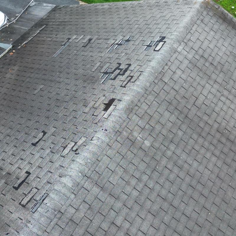 Asphalt shingle roof with extensive wind damage and missing patches Asphalt shingle roof with extensive wind damage and missing patches