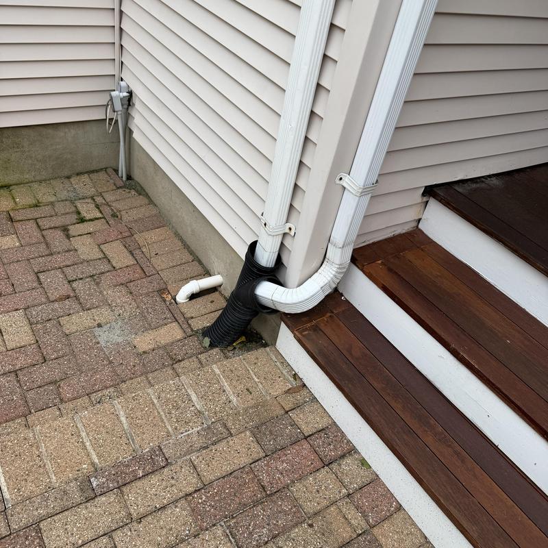 Downspout drainage pipes near wooden steps and brick patio Downspout drainage pipes near wooden steps and brick patio