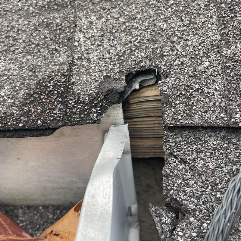 Asphalt shingle roof with torn and damaged edge near gutter