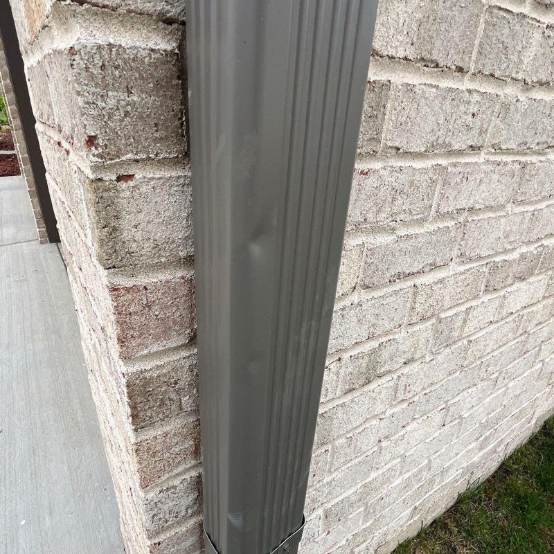 Downspout dented on brick exterior wall near sidewalk