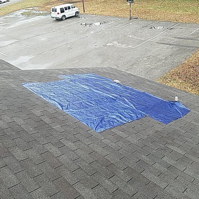 Shingle roof with storm damage covered by blue tarp