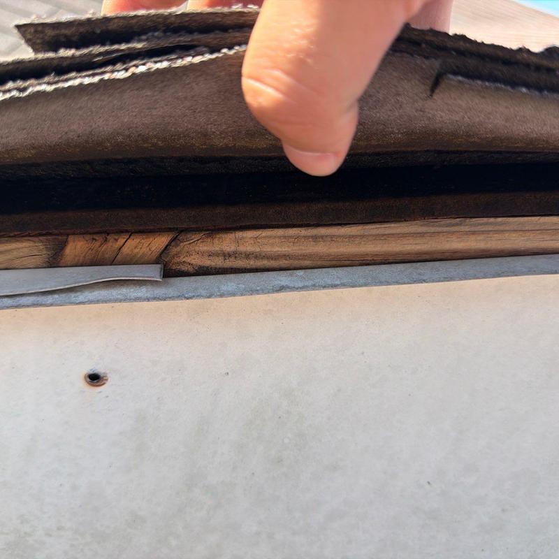 Roof decking exposed under lifted shingles during inspection