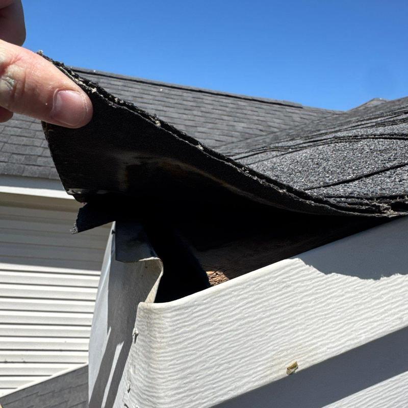 Roof shingles lifted showing underlying damage inspection