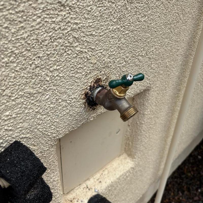 Outdoor water spigot on stucco wall with rust stain
