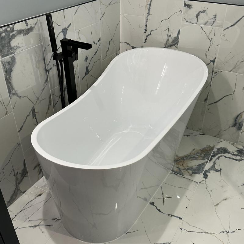 Freestanding bathtub with black floor-mounted faucet in marble bathroom