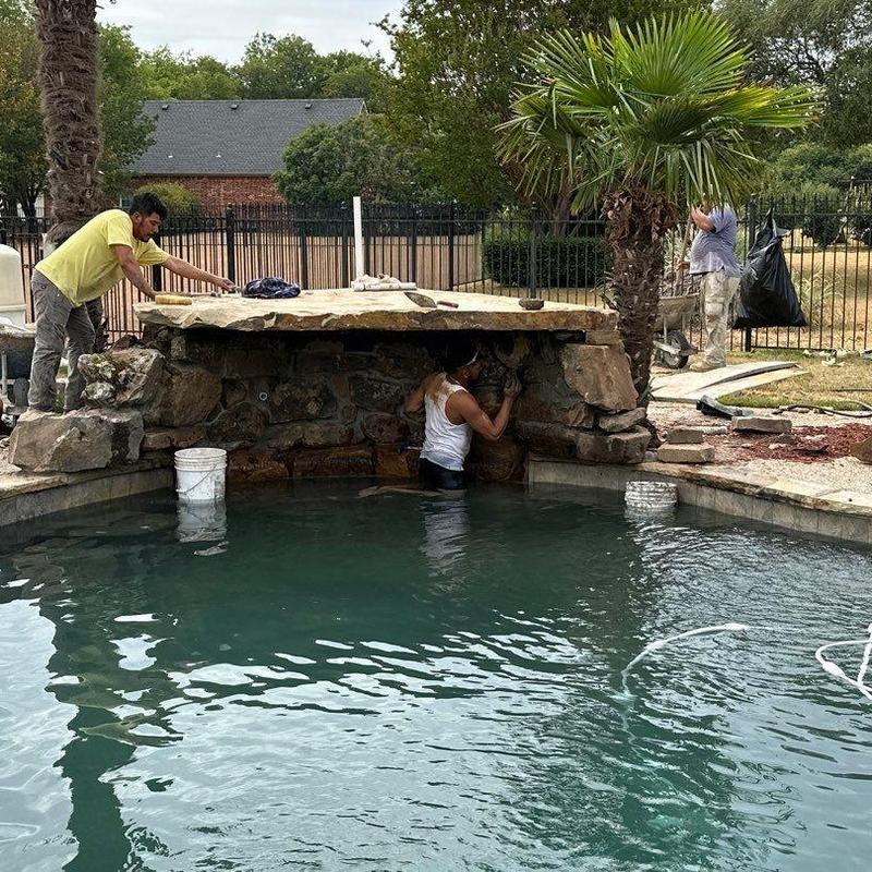 Natural stone waterfall repair beside pool in backyard Natural stone waterfall repair beside pool in backyard