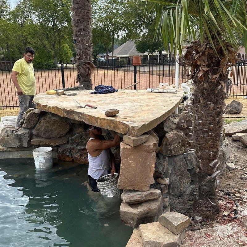 Natural stone waterfall repair beside backyard pool Natural stone waterfall repair beside backyard pool