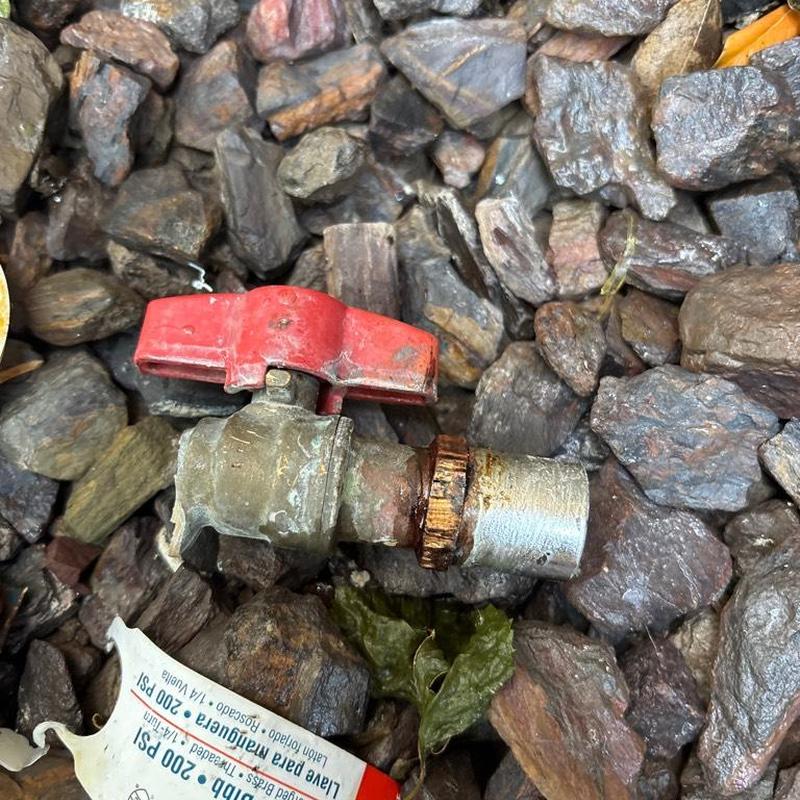 Hose bib valve with red handle on rocky ground
