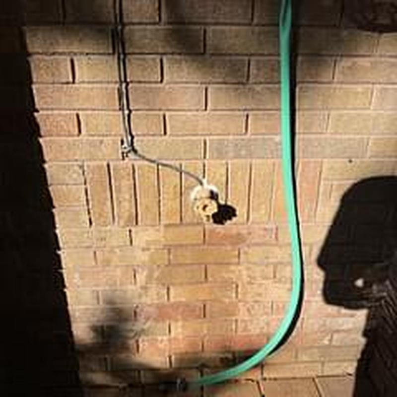 Hose bib with green garden hose on brick wall