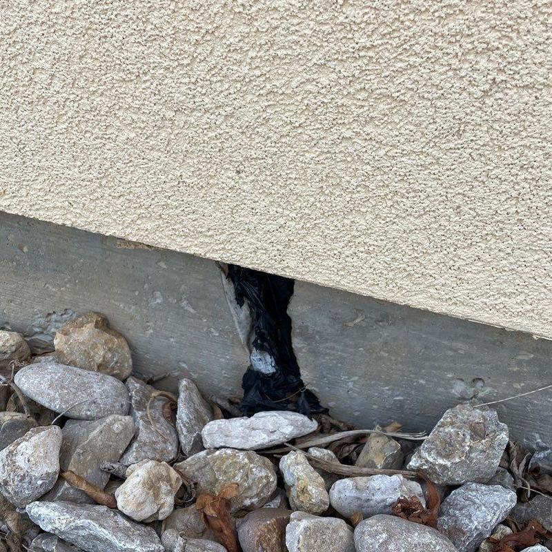 Stucco exterior wall base with visible damage and rocks Stucco exterior wall base with visible damage and rocks