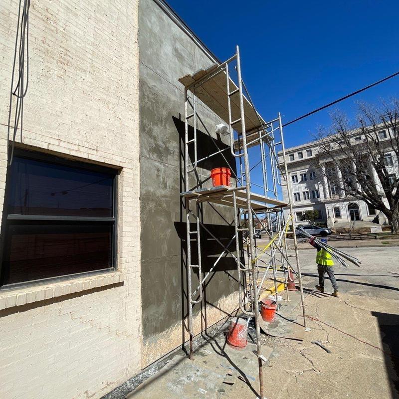 Stucco facade with scaffolding and worker carrying poles Stucco facade with scaffolding and worker carrying poles