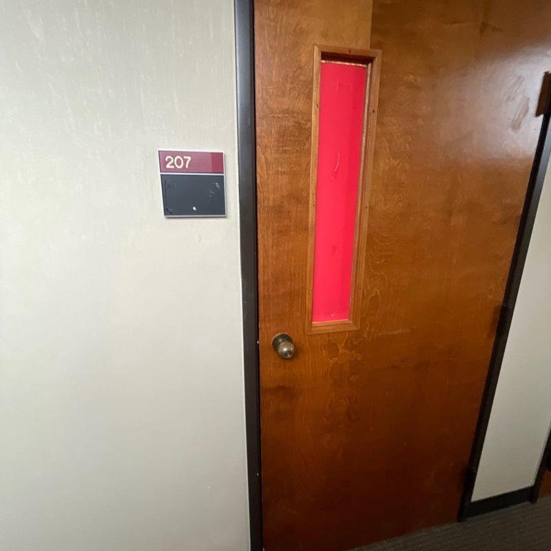Wooden door with narrow red window and room number sign Wooden door with narrow red window and room number sign