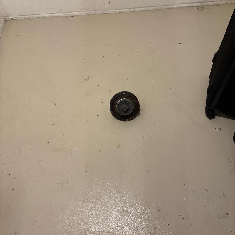 Floor drain cleanout plug on beige concrete floor