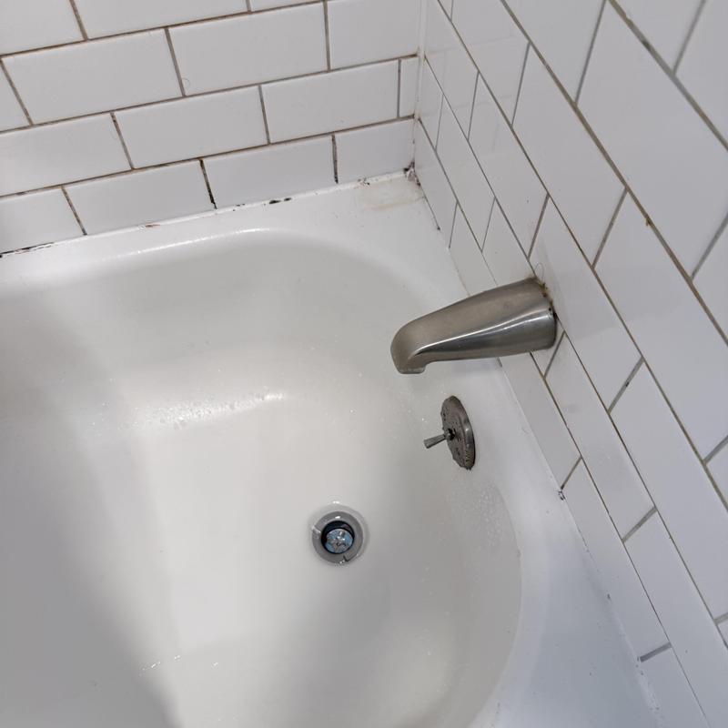 Tub drain with metal spout and white tile wall