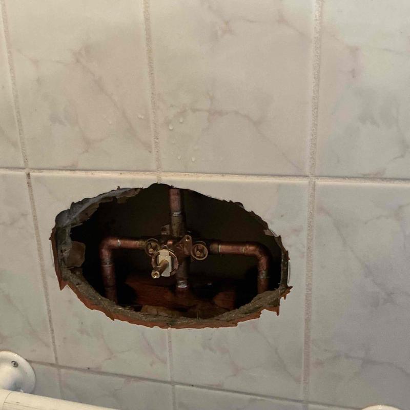 Two-handle shower valve with exposed plumbing behind tile wall