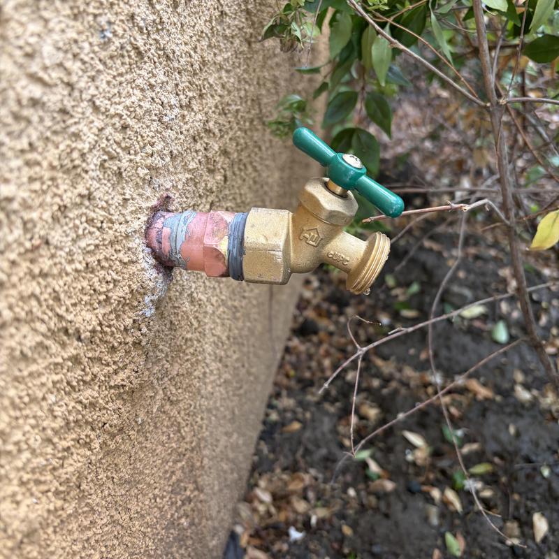 34-inch hose bib with green handle on stucco wall