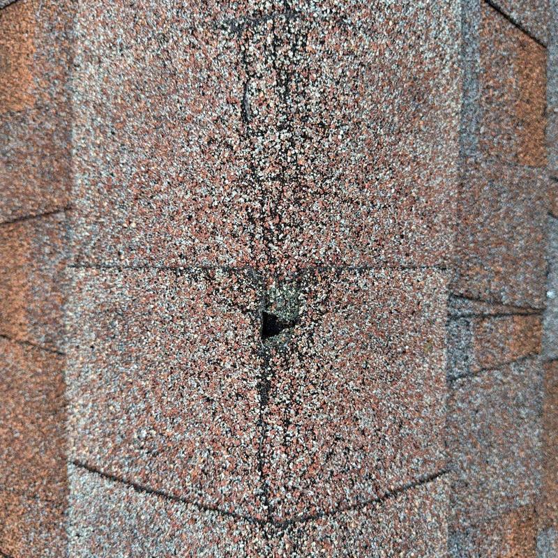 Asphalt roof shingle with hail damage hole close-up