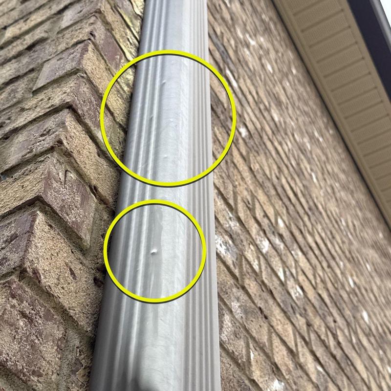 Metal downspout with dent damage on brick wall