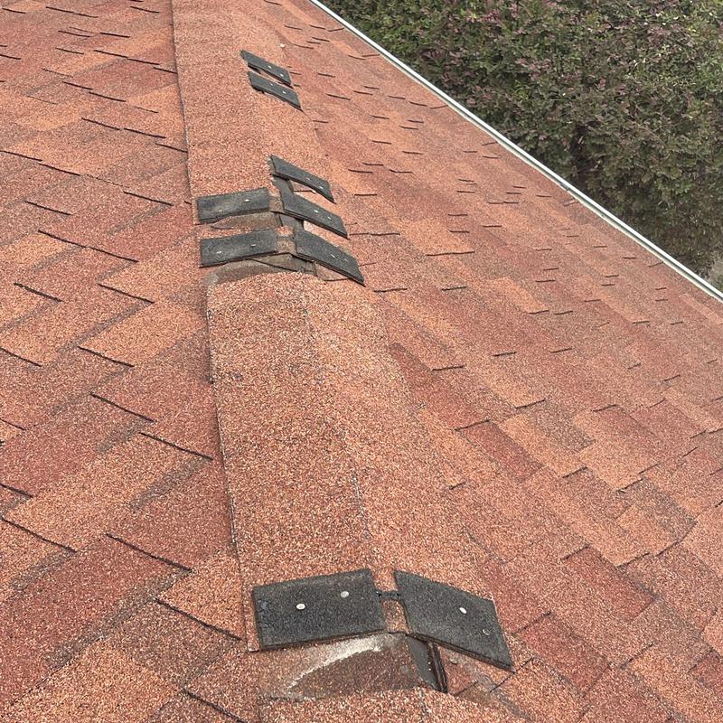 Asphalt shingle roof with damaged ridge caps after storm