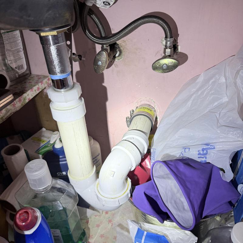 Lavatory drain pipes under sink with cleaning supplies nearby