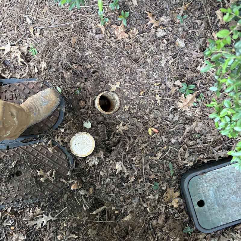 Water meter pit with exposed pipe and worker boots Water meter pit with exposed pipe and worker boots
