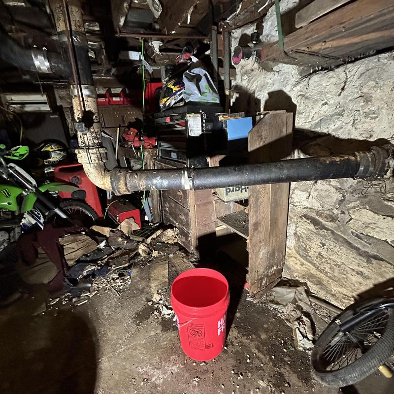 Cast iron sewer main in basement with red bucket Cast iron sewer main in basement with red bucket
