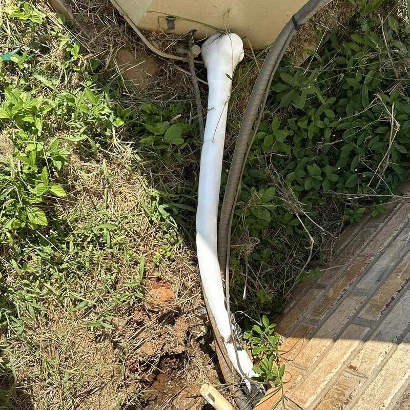 Drain line pipe with insulation beside brick wall outdoors Drain line pipe with insulation beside brick wall outdoors