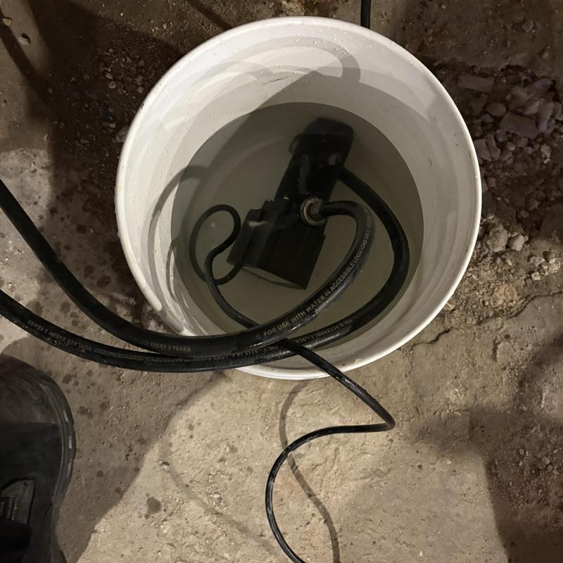 Sump pump submerged in water-filled bucket on basement floor