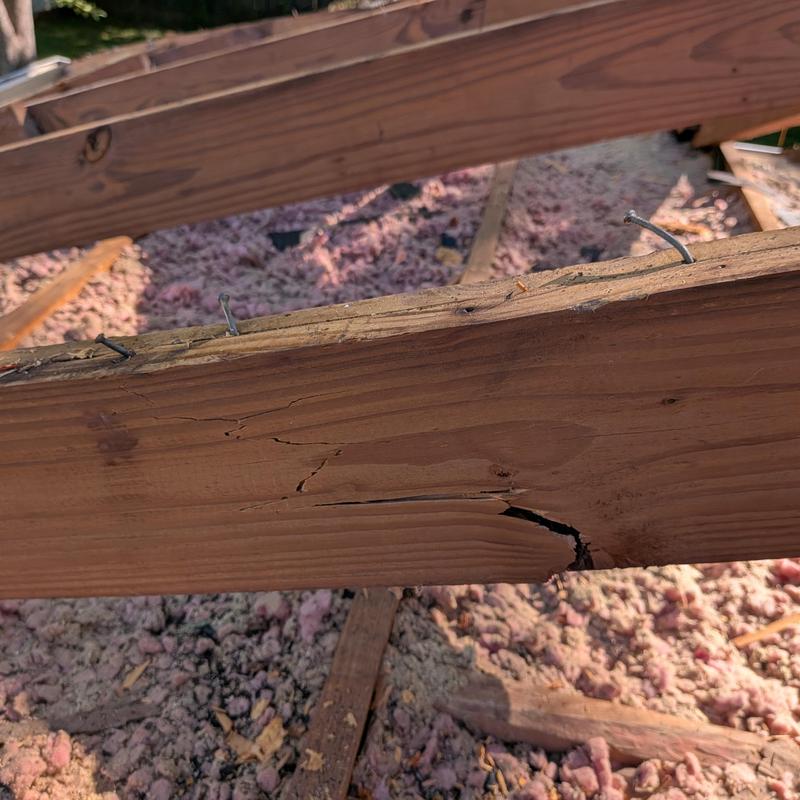 Damaged roof wood beam with cracks and nails
