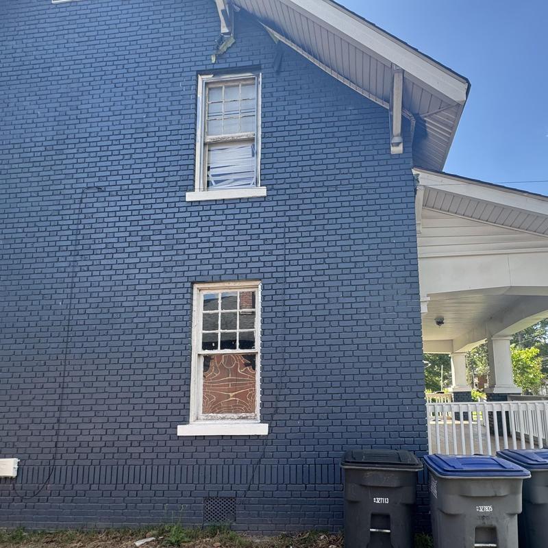 Brick exterior wall with damaged windows and trash bins