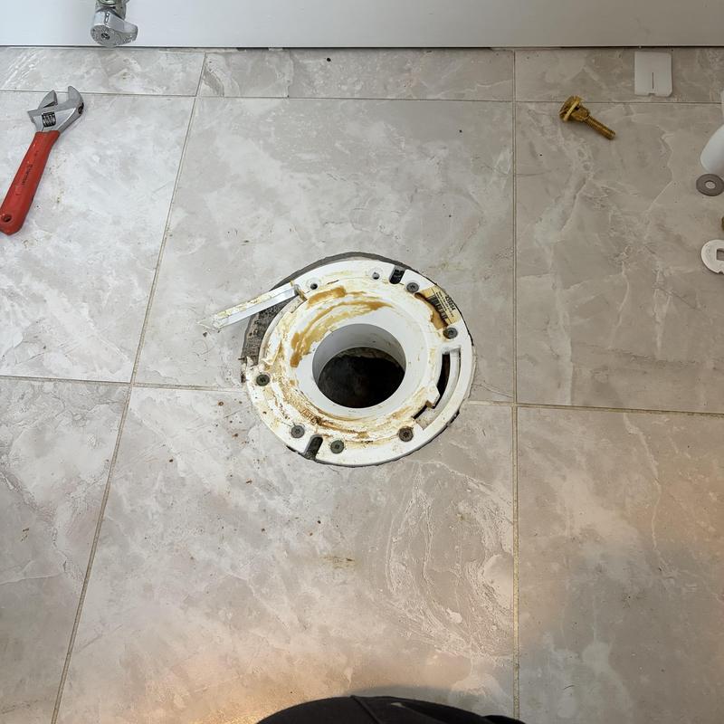 Toilet flange on tiled floor with wrench nearby